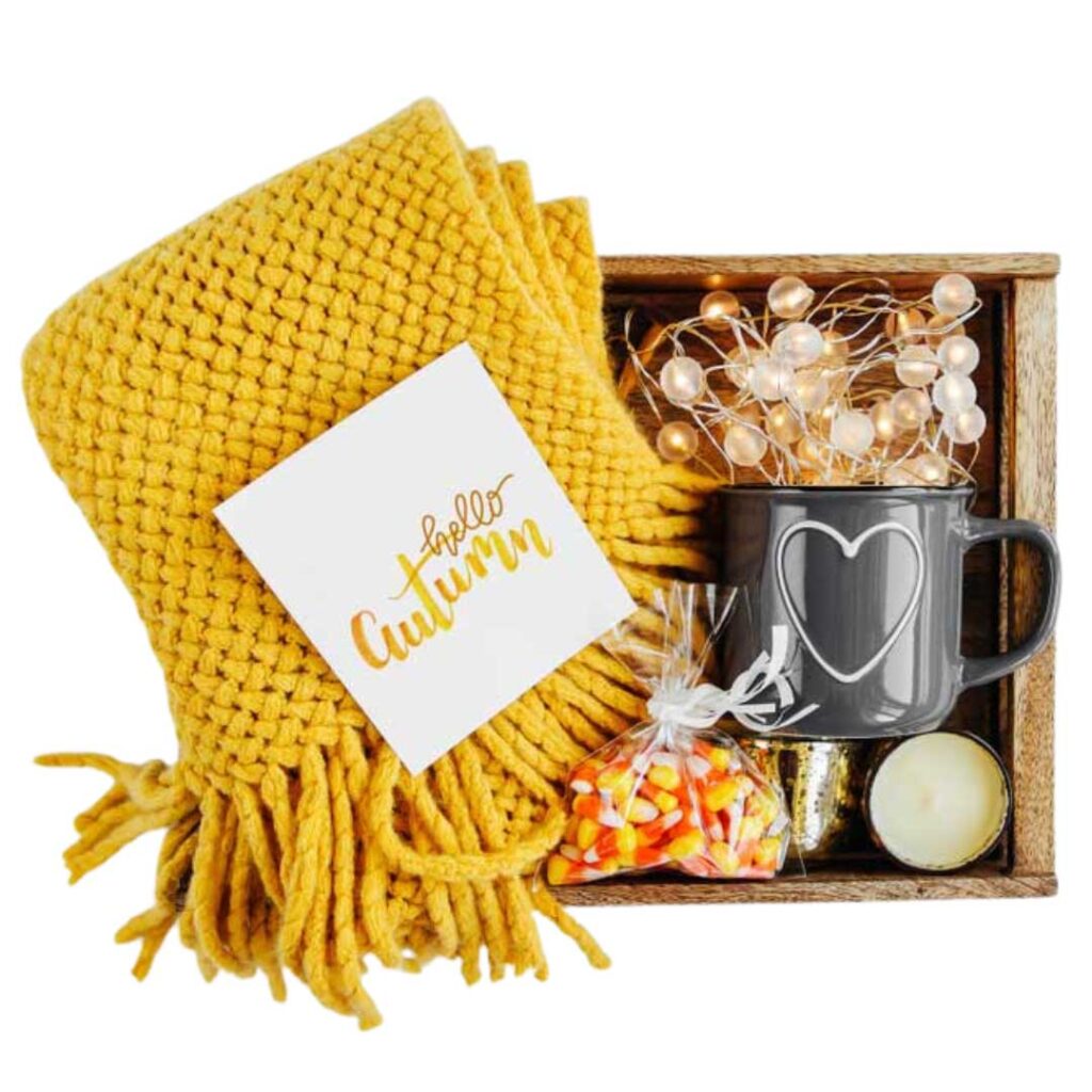 هدیه ی یک ماگ، چراغ های نورانی، آبنبات های خوشمزه و شال پاییزی خردلی و شمع در یک بسته ی کادویی 